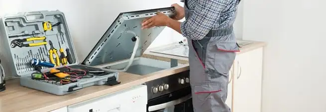Cooktop repair technician lifting a built-in stovetop for service in Clearwater, FL