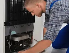 Refrigerator repair technician servicing the compressor and condenser area in Clearwater, FL